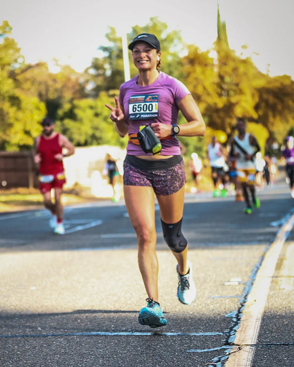 Coach Nicole running a marathon in a purple shirt, smiling and waving a peace sign